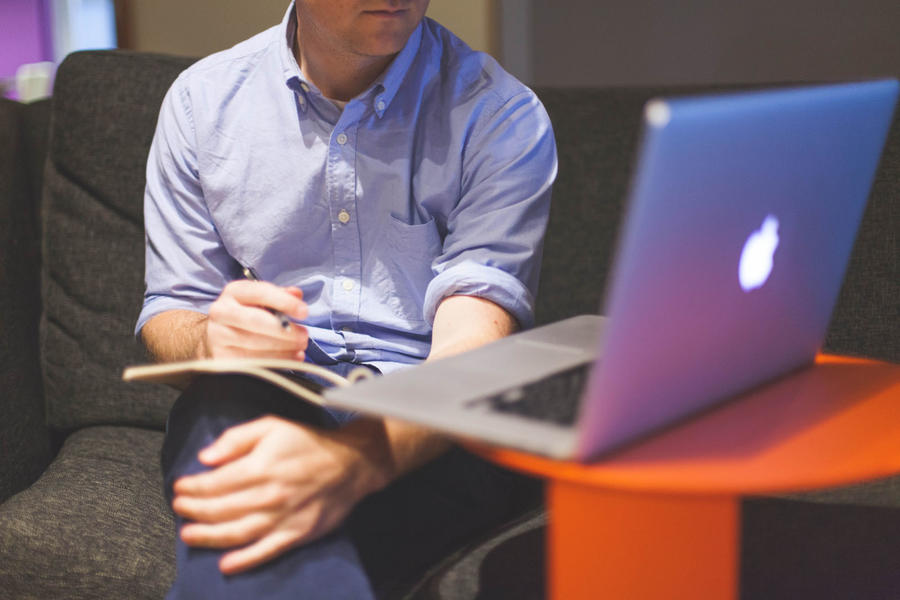 Person taking handwritten notes looking at Macbook laptop